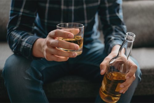 Мужчина сидит на диване с бутылкой и бокалом